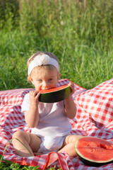 Cute dirty caucasian blonde baby girl eating fresh red watermelon at picnic in summer sunny weather. Healthy food for infant or kid loving fruit and berry concept. Vertical photo