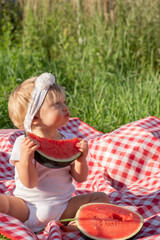 Cute dirty caucasian blonde baby girl eating fresh red watermelon at picnic in summer sunny weather. Healthy food for infant or kid loving fruit and berry concept. Vertical photo