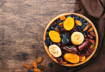 Dried fruits bowl. Healthy food snack: sun dried organic mix of apricots, figs, raisins, dates and other on wooden table, top view