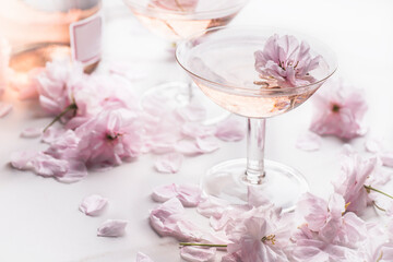 Romantic still life with rose wine in the two rare coupes champagne glasses with beautiful soft flowers, selective focus. Rose drink concept, pastel colors 