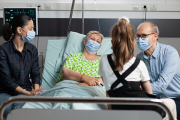 Family with protection face mask against coronavirus sitting with sick grandmother visiting during...