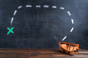 Wooden toy airplane biplane on the background of a chalk board with a drawing meaning the route and...
