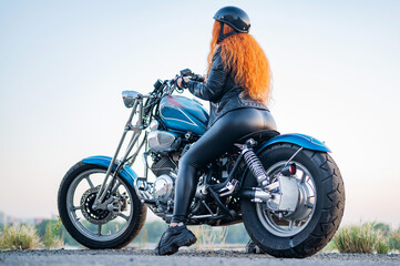 Fototapeta na wymiar Rear view of red-haired curly woman in helmet on motorcycle outdoors.