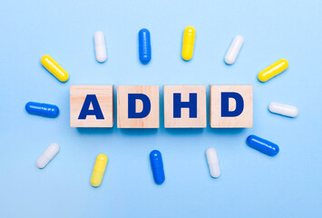 On a light blue background, multicolored pills and wooden cubes with the text ADHD. Medical concept