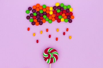 Multi-colored round candies are collected in the form of a cloud with rain on a lilac background, top view, flat lay