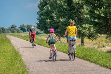 A father, mother and daughter are cycling on a Dutch dike. The little girl is wearing a pink...