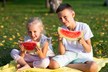 To cute kids lttle boy and girl eating juicy watermelon in the picnic at autumn park meadow.