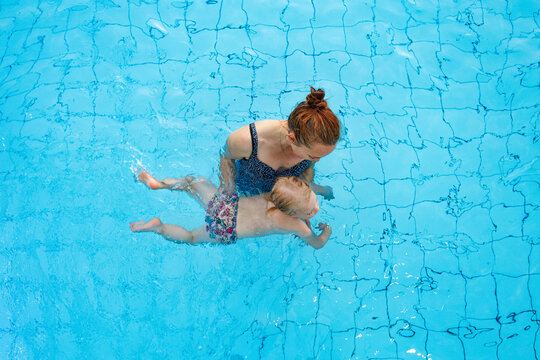 Happy family. Mom teaches her daughter 2-3 years old to swim in the pool. Top view.