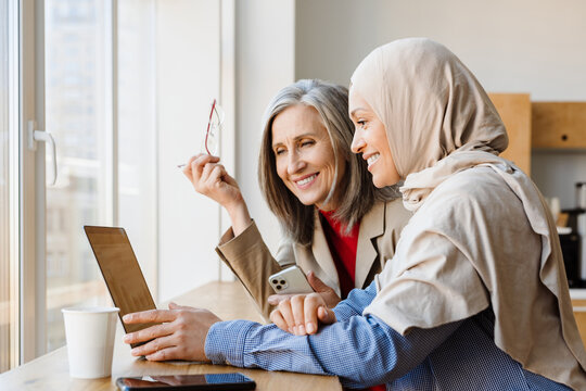 Multiracial two women working with laptop in office kitchen