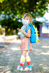 Naklejka premium Little toddler girl on her first day on way to playschool with medical mask against corona covid virus. Healthy beautiful baby walking to nursery preschool and kindergarten. Happy child with backpack