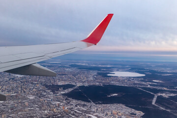 Fototapeta na wymiar a view of the winter city from a height of flight from the window of an airplane with a silvery red wing