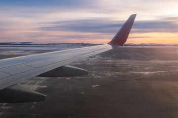 view from the airplane window of the airport runway and part of the silvery red wing during takeoff