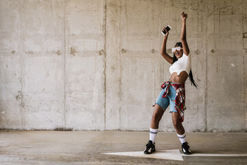 Black young woman dancing and smiling while using mobile phone
