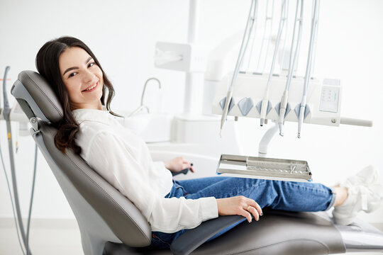 Image of satisfied young woman sitting in dental chair at medical center while professional doctor