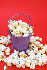 The fresh popcorn in a small decorative iron bucket on a red background.