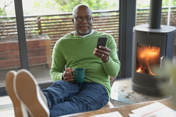 Relaxing senior african american man siting and using smartphone in the modern living room