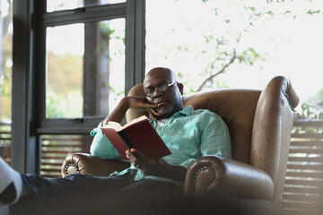 Senior african american man sitting on the armchair and reading book in the modern living room