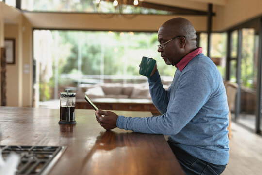 Senior african american man drinking coffee and using tablet in the modern kitchen