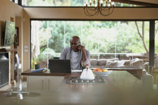 Senior african american man working on laptop and using smartphone in the modern kitchen