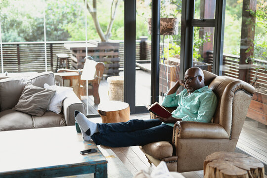 Relaxing senior african american man sitting and reading book in the modern living room