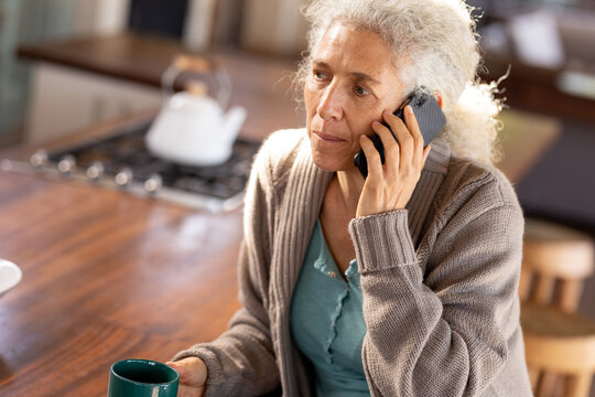 Relaxing senior caucasian woman in the kitchen using smartphone and drinking coffee