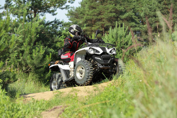 Man driving modern quad bike on sandy road near forest. Extreme sport