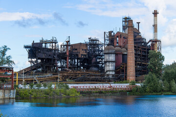 The building of the old factory on the river bank. Iron smelter against the blue sky.