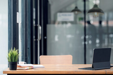 Rear view of tablet with keyboard and supplies on wooden table in dark office room.