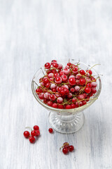 Frozen red currants in a glass vase on a white wooden table. Close-up.