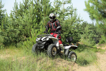 Man driving modern quad bike on sandy road near forest. Extreme sport