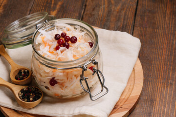Homemade sauerkraut with carrots, cranberries and pepper on dark wood background.
