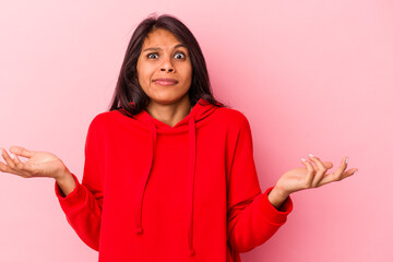 Young latin woman isolated on pink background doubting and shrugging shoulders in questioning...