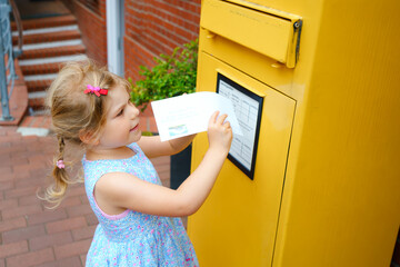 Little preschool girl throwing letter in a mailbox. Excited child writing card or letter for...