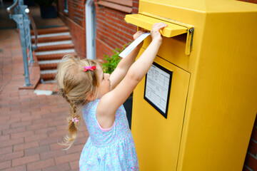 Little preschool girl throwing letter in a mailbox. Excited child writing card or letter for...