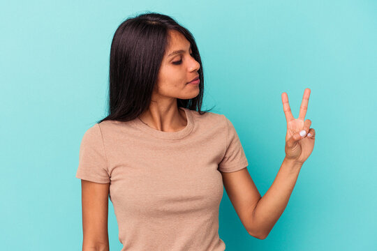 Young latin woman isolated on blue background joyful and carefree showing a peace symbol with fingers.