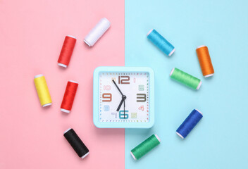 Alarm clock with Skeins of colored thread on blue-pink pastel background. Hobby time