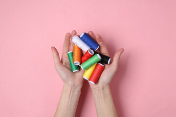 Hand holding Skeins of colored thread on pink pastel background