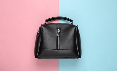 Naklejka premium Fashionable leather black handbag on pink blue pastel background. Top view