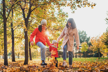 Fototapeta premium Mother and daughter having fun in the autumn park among the falling leaves. Active lifestyle