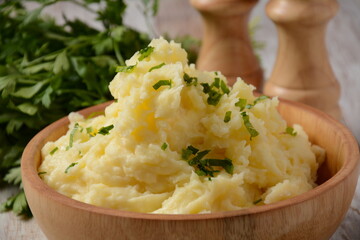 Fresh homemade creamy mashed potato in bowl, on wooden table with herbs