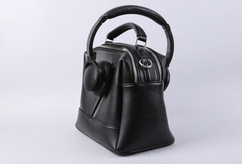 Stylish black leather handbag with headphones on gray background