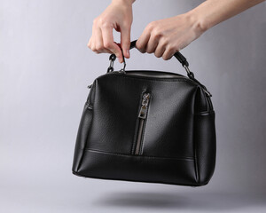 Woman's hand opens black leather bag on gray background