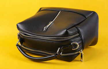 Stylish black leather handbag on yellow background