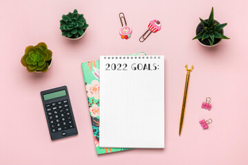 open notepad with text Goals 2022 goals, succulents, golden pen on pink background, spiral notebook on table Business, planning, education concept