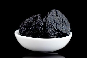 Several sweet dark prunes in a ceramic bowl, close-up, isolated on black.