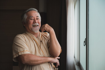 asian senior look through the window, keep smiling while stay in the hospital ward, happy great attitude pateint during medical treatment, white hair olderly, health care concept.