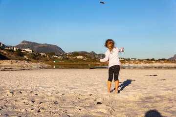 A small girl throws a stick while playing on the beach at Noordhoek, Cape Town.