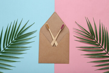 Eco concept. Craft envelope and wooden toothbrushes on blue pink backgroundwith palm leaves