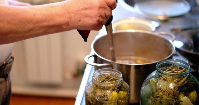An elderly man pours brine into prepared cucumber jars. Homemade preparations