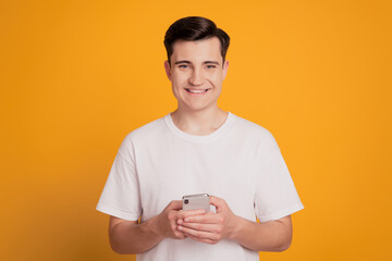 Portrait of cheerful guy hold smartphone beaming shiny smile on yellow background
